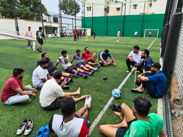 Club friends sitting together on the turf, with a football beside them, sharing a relaxed conversation.
